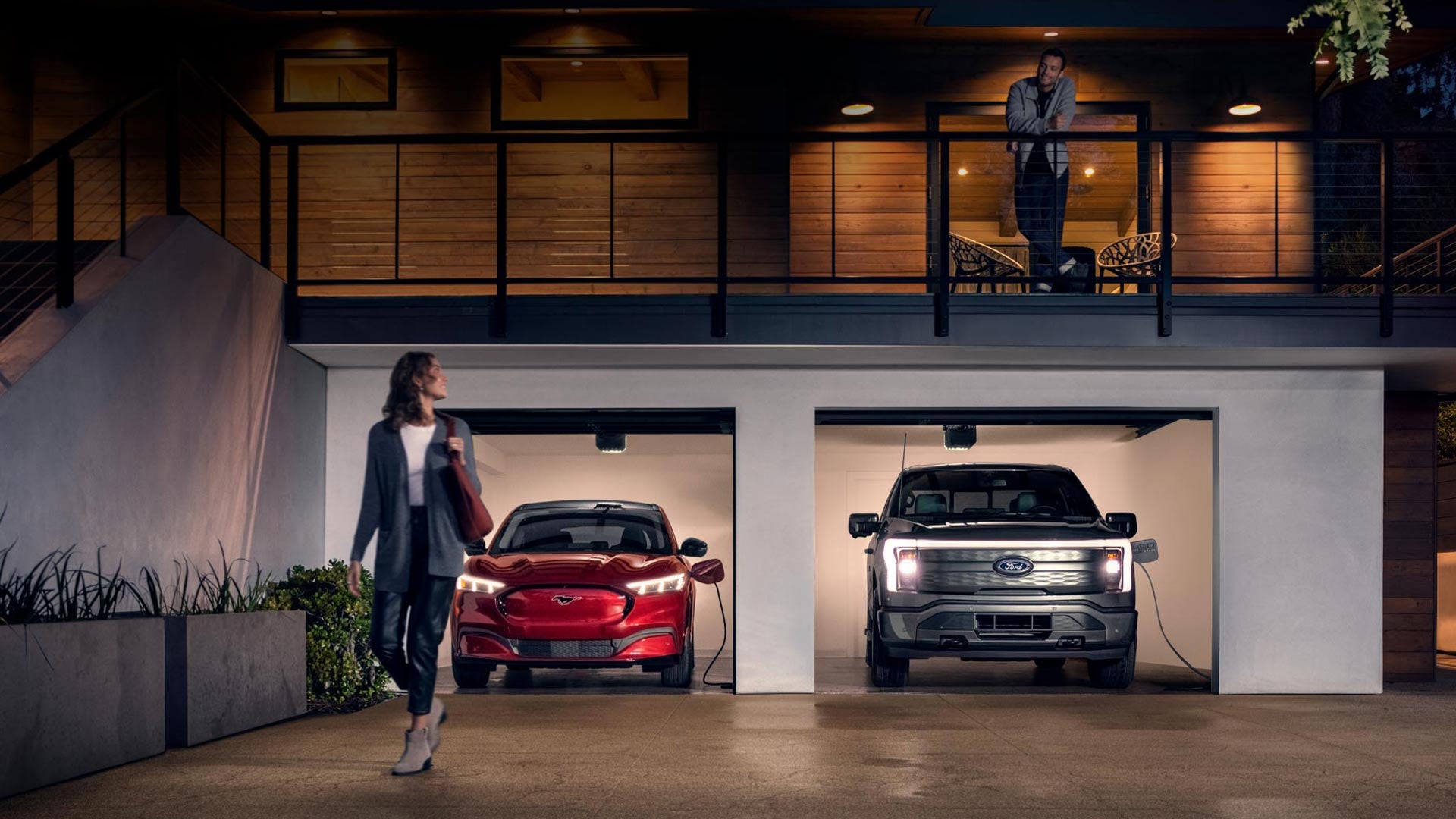 Woman walking out from home garage with a 2024 Mustang® Mach-E and Ford Lightning® truck in plugged-in and charging | Lundgren Ford in Eveleth MN