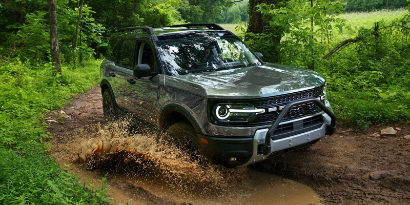A 2026 Ford Bronco navigates a muddy trail, showcasing its off-road capabilities and rugged design.