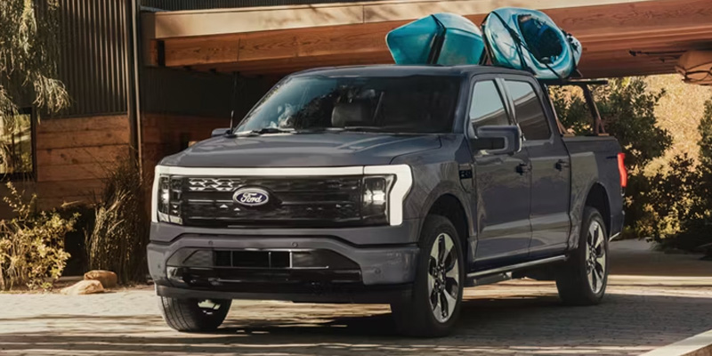 A gray Ford truck parked outside with kayaks on its roof rack.